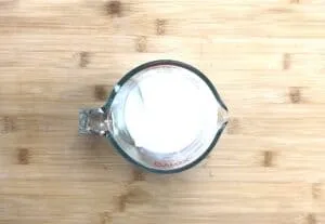 Glass measuring cup filled with white liquid, on a wooden surface. Perfect for baking recipes.